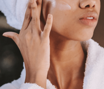 Une femme appliquant une crème hydratante sur sa joue, avec une serviette sur la tête.